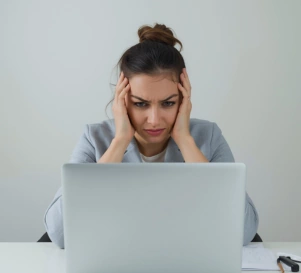 Unternehmerin stützt mit beiden Händen ihren Kopf und schaut verzweifelt auf ihren Laptop