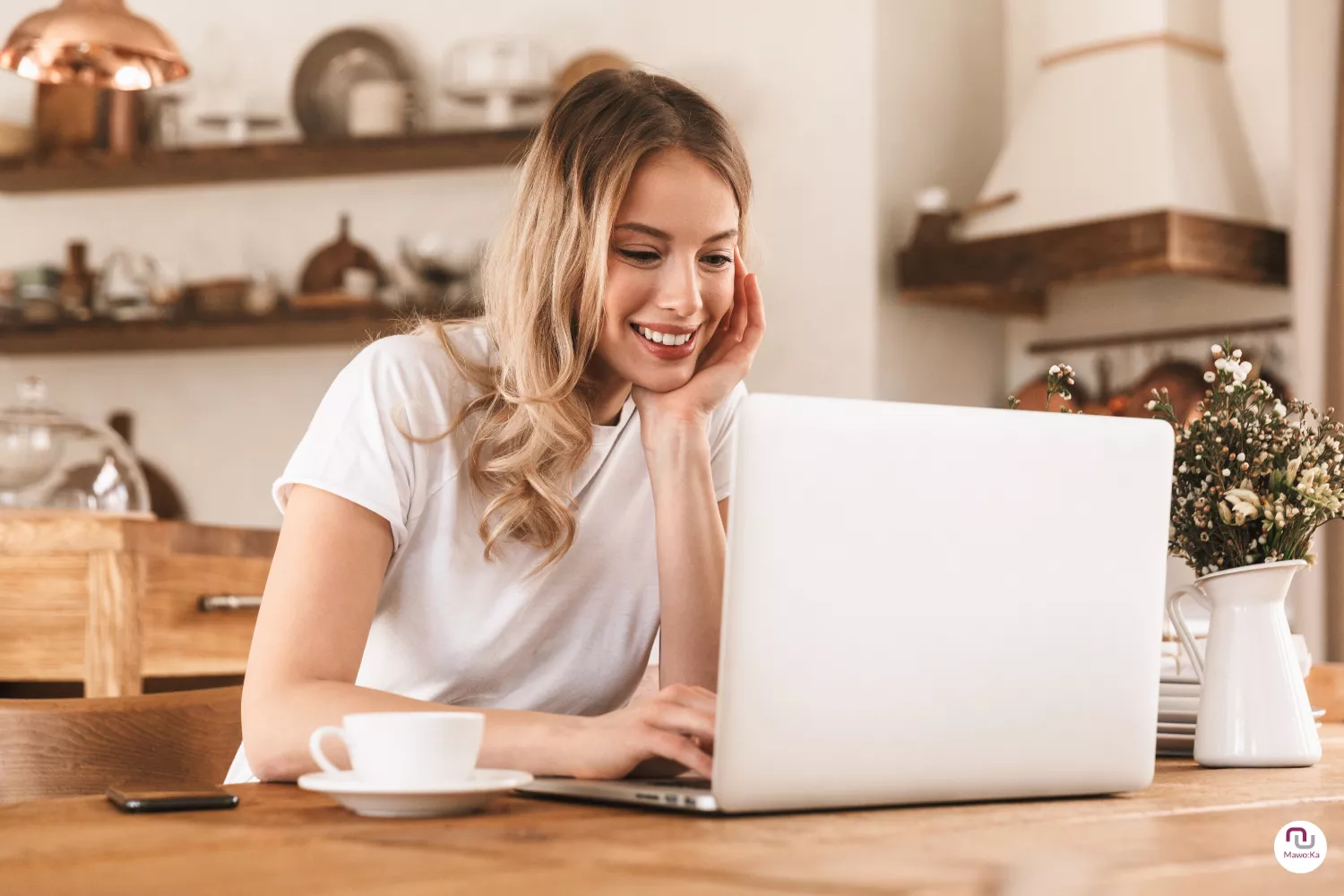 Junge Soloselbstständige sitzt am Laptop mit einer Tasse Kaffee und lächelt