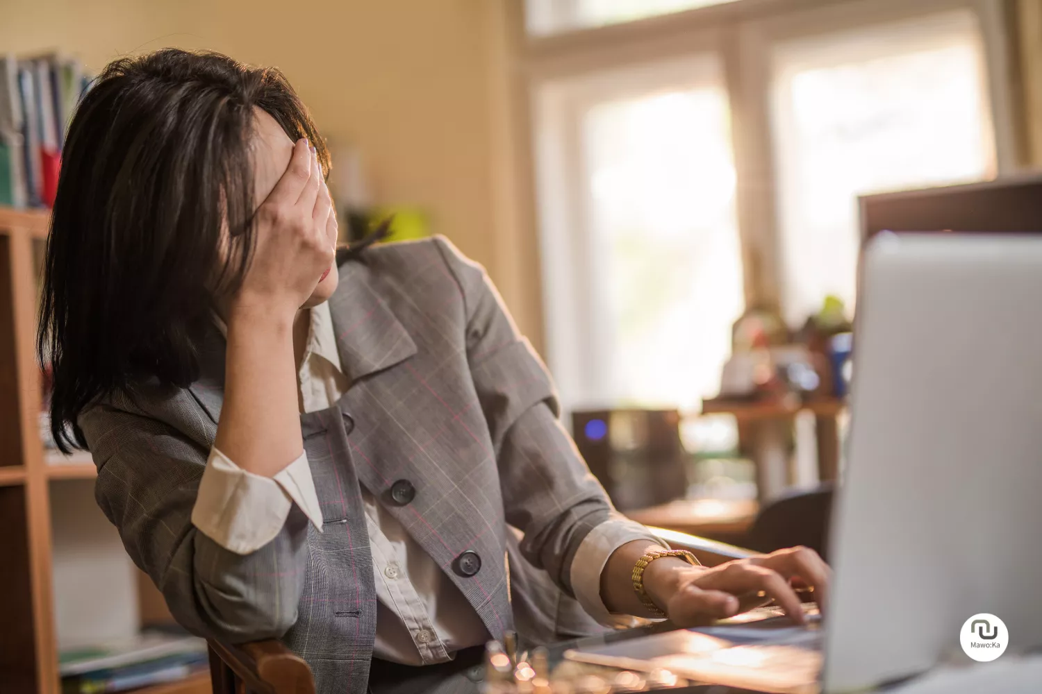 Soloselbstständige Frau überfordert mit Social Media und hält eine Hand vor ihr Gesicht und hat die andere Hand auf der Tastatur ihres Laptops